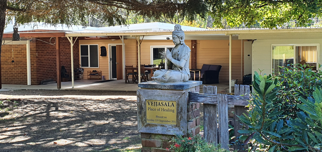 The front of Vejjasala retreat centre with a statue of the Buddha and trees shading the area